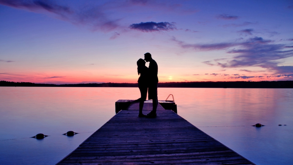 日落湖畔夫妇浪漫拥吻壁纸。